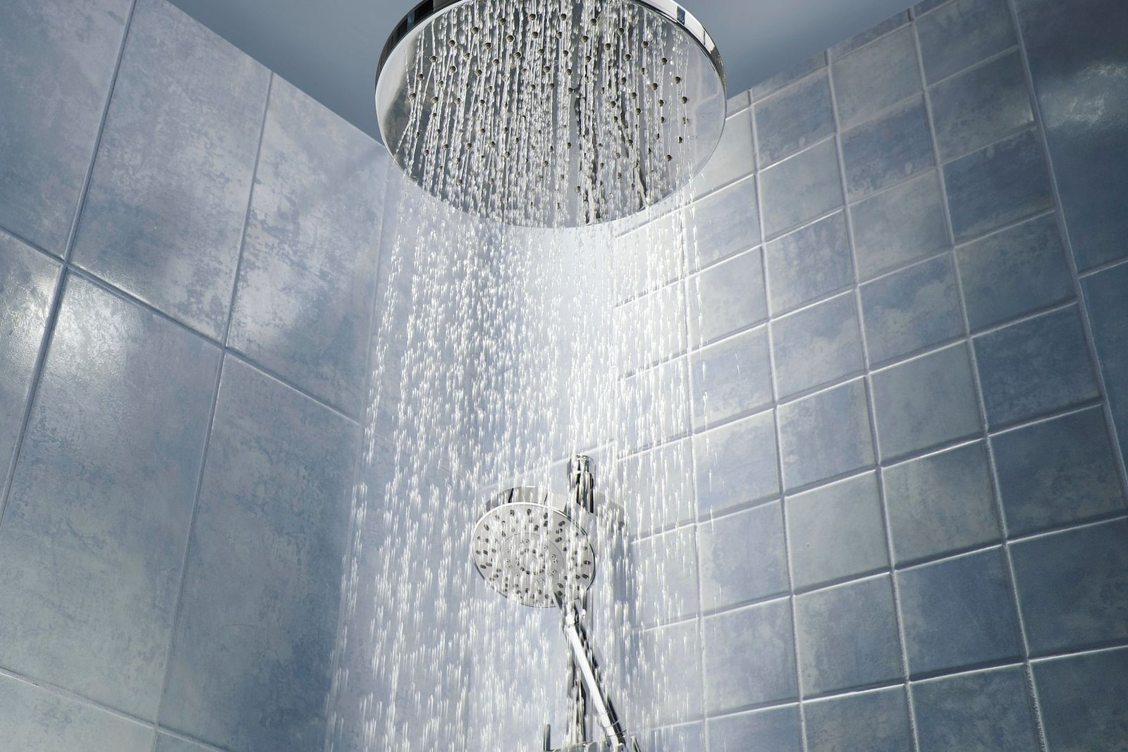 Ceiling shower and hand shower with water falling on bathroom tiles